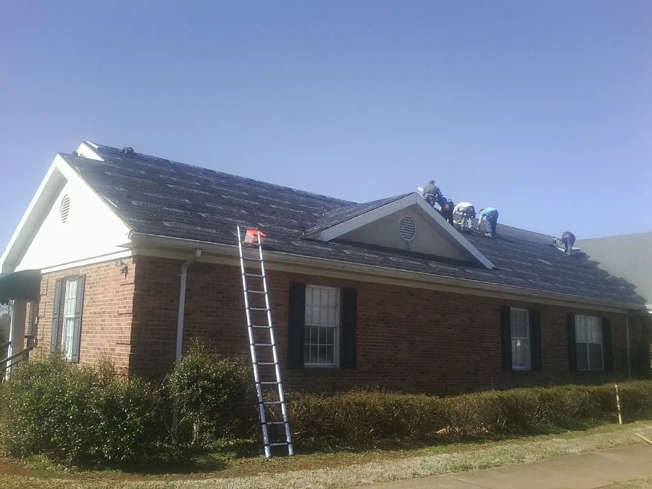 Crew tearing shingles off a brick ranch roof with a ladder set — Emergency Roof Repair work by our crew in Maitland