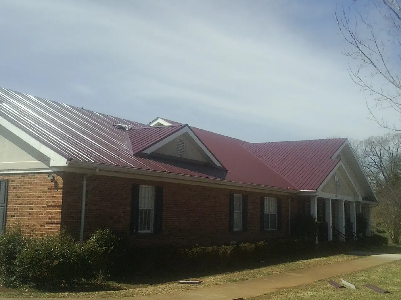Red metal roof with gabled entries on a long brick building, from a Hail Damage Roof Repair job in Maitland