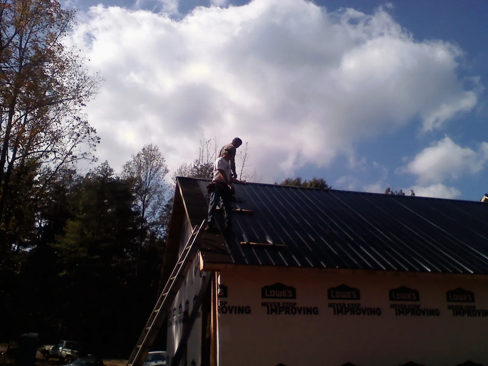 Roofer fastening dark metal panels high against a cloudy sky, from a Roof Inspection job in Maitland